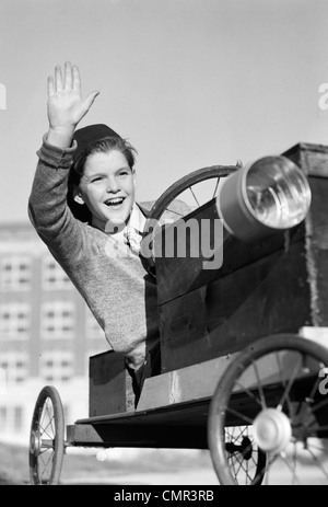 1940s BOY IN HOMEMADE RACE CAR GO-CART SMILING AND WAVING SOAPBOX DERBY Stock Photo