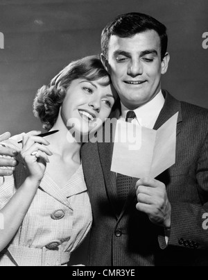 1960s COUPLE READING LETTER HAPPY WOMAN RESTING HEAD ON MANS SHOULDER Stock Photo