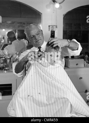 1950s BOY IN BARBERSHOP GETTING HIS HAIR CUT Stock Photo