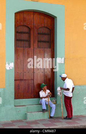 Two elderly men talking at the steps of a large wooden door Stock Photo