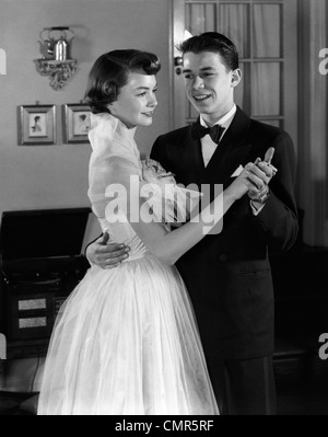 1950s SMILING TEENAGE COUPLE IN FORMAL EVENING WEAR DANCING INDOORS Stock Photo