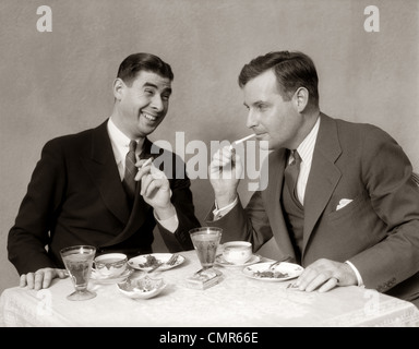 1930s TWO MEN LIGHTING AFTER DINNER CIGARETTES SMILING Stock Photo