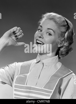 1950s 1960s WOMAN HOUSEWIFE IN APRON SMILING PROUDLY POINTING AT HERSELF WITH THUMB Stock Photo