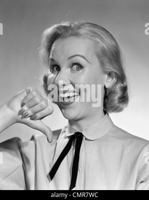 1950s WIDE-EYED SMILING BLOND PORTRAIT WOMAN POINTING TO HERSELF WITH THUMB, LOOKING AT CAMERA Stock Photo