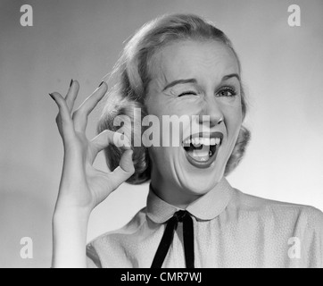 1950s BLOND WOMAN WINKING EYE AND MAKING OK SIGN WITH THUMB AND FINGER Stock Photo