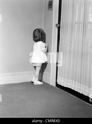 1950s 1960s LITTLE GIRL IN WHITE DRESS BEING PUNISHED STANDING IN A CORNER Stock Photo