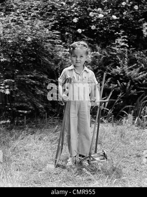 1940s CHILD HOLDING LAWN TOOLS WORK CLOTHES GRASS Stock Photo