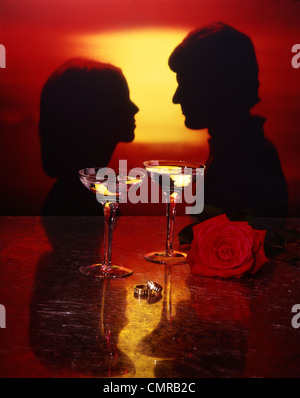 1970s PORTRAIT SILHOUETTE OF COUPLE MAN WOMAN AT SUNSET GOLD ENGAGEMENT WEDDING RINGS WINE GLASSES RED ROSE Stock Photo