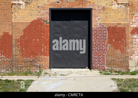 Big metal door in an old brick warehouse with city sidewalk in front Stock Photo