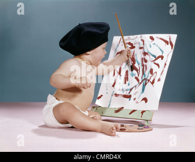 1960s BABY ARTIST WEARING BLACK BERET SITTING IN FRONT OF EASEL PAINTING Stock Photo