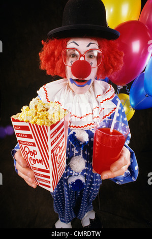 1980s 1990s CLOWN WITH GLASSES AND HAT HOLDING POPCORN AND DRINK LOOKING AT CAMERA Stock Photo