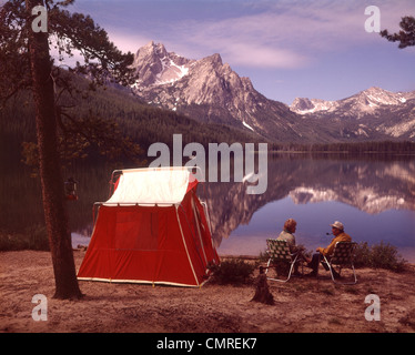 1970s OLDER COUPLE SITTING CAMPING BY RED TENT STANLEY LAKE IDAHO Stock Photo