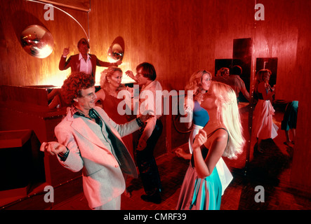 1970s 1980s COUPLES MEN WOMEN DANCING DISCO DISCOTHEQUE INDOOR DJ IN BACK Stock Photo