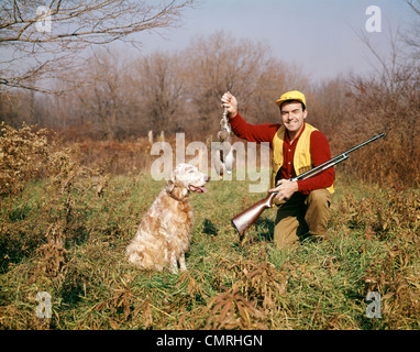 1950s MAN WITH HUNTING DOG AND GUN HOLDING UP BRACE OF BIRDS LOOKING AT CAMERA Stock Photo