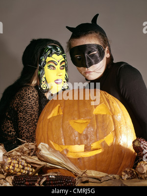 1960s TWO YOUNG GIRLS IN WITCH AND BLACK CAT HALLOWEEN COSTUMES WITH CARVED JACK-O-LANTERN PUMPKIN Stock Photo