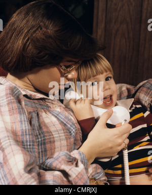 1970s TEENAGE GIRL BABY SITTER LETTING SMALL HAPPY BOY TALK ON TELEPHONE Stock Photo