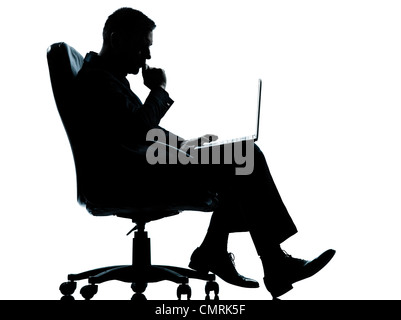 one caucasian business man computer computing serious sitting in armchair silhouette Full length in studio isolated on white background Stock Photo