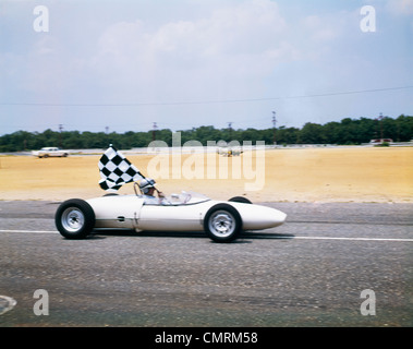 1960s RACE CAR DRIVER IN LOTUS FORD CAR TAKING VICTORY LAP HOLDING CHECKERED FLAG RETRO Stock Photo