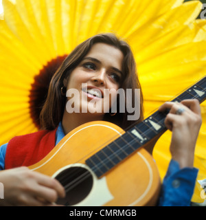 1970 1970s RETRO SMILING TEENAGED GIRL PLAYING ACOUSTIC GUITAR MUSICIAN LARGE SUNFLOWER BACKDROP Stock Photo