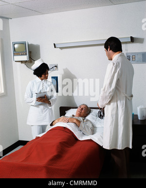 1970s MAN DOCTOR WOMAN NURSE OBSERVING MALE PATIENT CHECKING VITAL ...