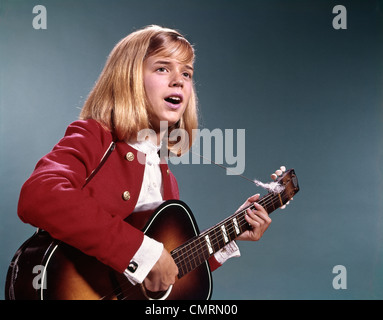 1960 1960s RETRO BLONDE TEENAGED GIRL SINGING AND PLAYING ACOUSTIC GUITAR Stock Photo