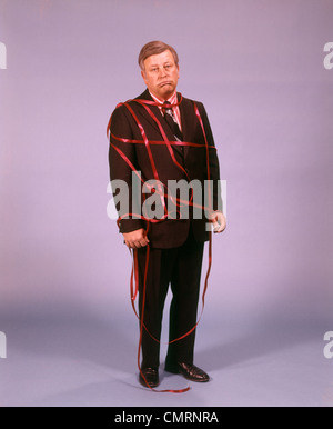 1970 1970s MIDDLE AGED MAN BUSINESS SUIT DISAPPOINTED DEPRESSED UNHAPPY RED TAPE RIBBON TIED UP Stock Photo