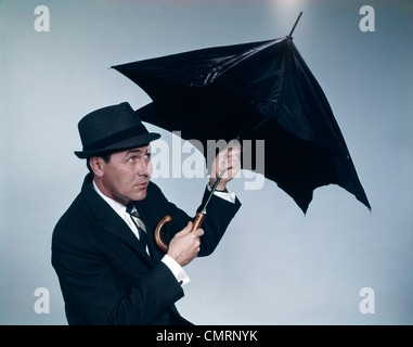 BUSINESSMAN WEARING HAT OPENING UMBRELLA TO PROTECT FROM RAIN STUDIO Stock Photo