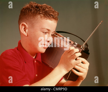 1960 1960s YOUNG PRETEEN BOY LISTENING TO PORTABLE TRANSISTOR RADIO HELD UP BY EAR FACE RADIOS TRANSISTORS RETRO Stock Photo