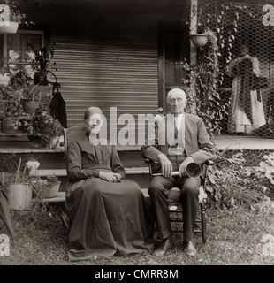 1890s 1900s PORTRAIT SENIOR COUPLE SEATED IN GARDEN MAN HOLDING EAR TRUMPET Stock Photo