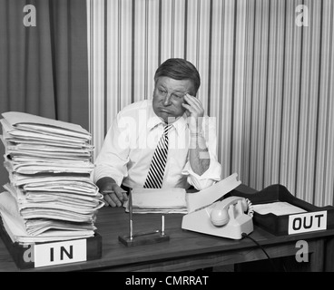 1970s CONCERNED BUSINESSMAN STARING LARGE PILE PAPERWORK IN IN-BOX Stock Photo