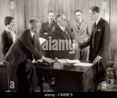 1930s GROUP BUSINESS MEN AND WOMAN IN OFFICE BOSS SHAKING HANDS WITH NEW HIRE Stock Photo