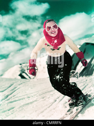 1940s 1950s SMILING WOMAN SKIING DOWNHILL WEARING GOGGLES RED HOOD AND RED GLOVES Stock Photo