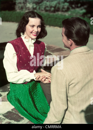 1940s 1950s SMILING TEEN COUPLE SITTING BY WELL HOLDING HANDS Stock Photo