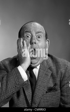 1960s PORTRAIT OF BALDING MAN HOLDING HAND UP TO FACE WITH SHOCKED EXPRESSION EYES BULGING LOOKING AT CAMERA & MOUTH OPEN Stock Photo