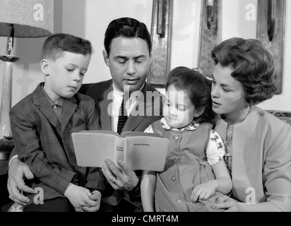 1960s FAMILY MOTHER FATHER SON DAUGHTER SITTING TOGETHER READING BIBLE INDOOR Stock Photo