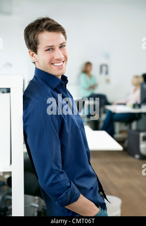 Portrait of smiling man leaning on bookshelf Stock Photo