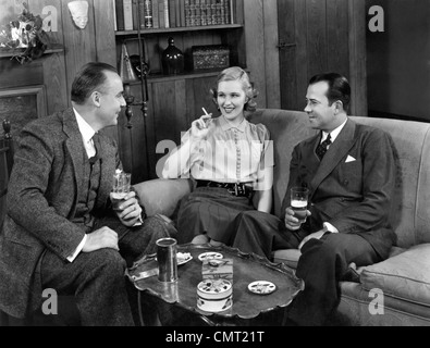 1940s TWO MEN AND ONE WOMAN SOCIAL GROUP SITTING ON COUCH DRINKING BEER SMOKING CIGARETTES TALKING Stock Photo