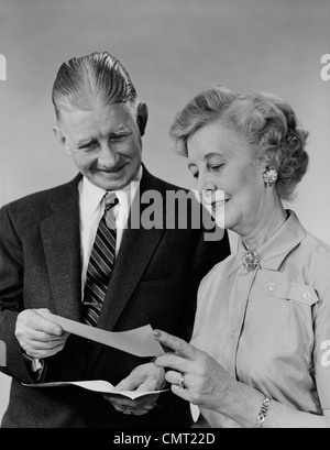 1960s SENIOR COUPLE MAN WOMAN READING HOLDING CHECK Stock Photo