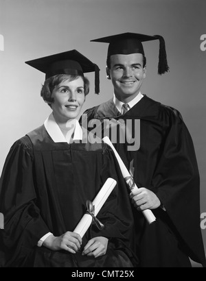 1960s PORTRAIT COUPLE MAN WOMAN IN GRADUATION ROBES HOLDING DIPLOMAS SMILING Stock Photo