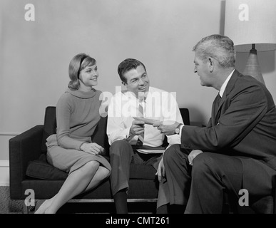 1960s COUPLE SITTING ON COUCH TALKING TO  SALESMAN Stock Photo