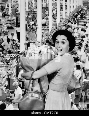 1960s HOUSEWIFE LOOKING AT CAMERA HOLDING GROCERY BAG SUPERIMPOSED OVER GROCERY STORE CHECK-OUT LINES Stock Photo