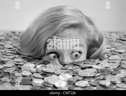 1960s BUG-EYED SURPRISED WOMAN BURIED IN COINS MONEY SYMBOLIC Stock Photo