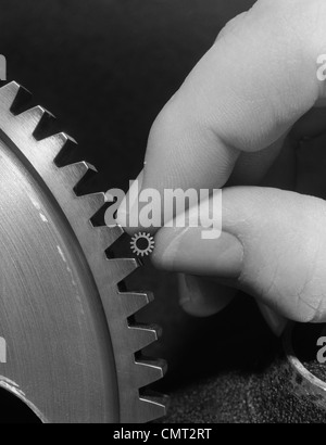 1970s HANDS HOLDING TINY GEAR ALONGSIDE LARGER GEAR Stock Photo