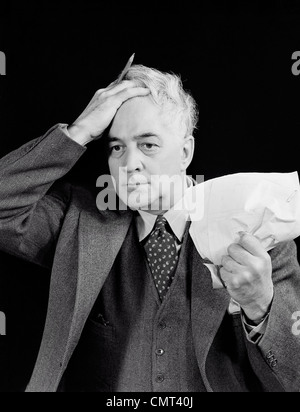 1940s OLDER MAN CRUMPLED PAPER IN ONE HAND HOLDING OTHER HAND TO HEAD FRUSTRATED EXPRESSION INDOOR Stock Photo