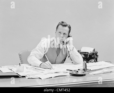 1930s 1940s YOUNG BUSINESSMAN SITTING AT DESK TALKING ON TELEPHONE TYPEWRITER WEARING VEST HOLDING PENCIL SHIRTSLEEVES Stock Photo