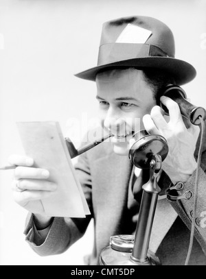 1930s MAN EXCITED NEWSPAPER REPORTER SMOKING PIPE PRESS PASS IN HAT TALKING ON UPRIGHT PHONE REPORTING STORY FROM NOTE PAD Stock Photo
