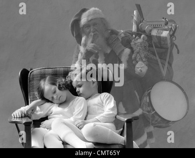 1930s SANTA CLAUS FINGER TO LIPS SACK OF CHRISTMAS TOY PRESENTS OVER SHOULDER GHOST BEHIND BOY AND GIRL ASLEEP IN CHAIR Stock Photo