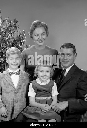 1950s 1960s FAMILY PORTRAIT SMILING FATHER MOTHER DAUGHTER SON SITTING TOGETHER IN FRONT OF INDOOR CHRISTMAS TREE Stock Photo