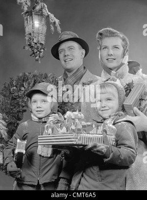1950s 1960s FAMILY BY LANTERN CARRYING WRAPPED CHRISTMAS PRESENTS Stock Photo