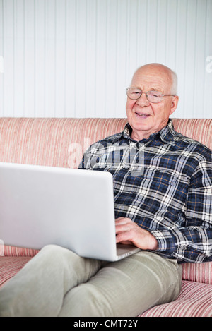 Elderly man sitting on sofa with laptop Stock Photo